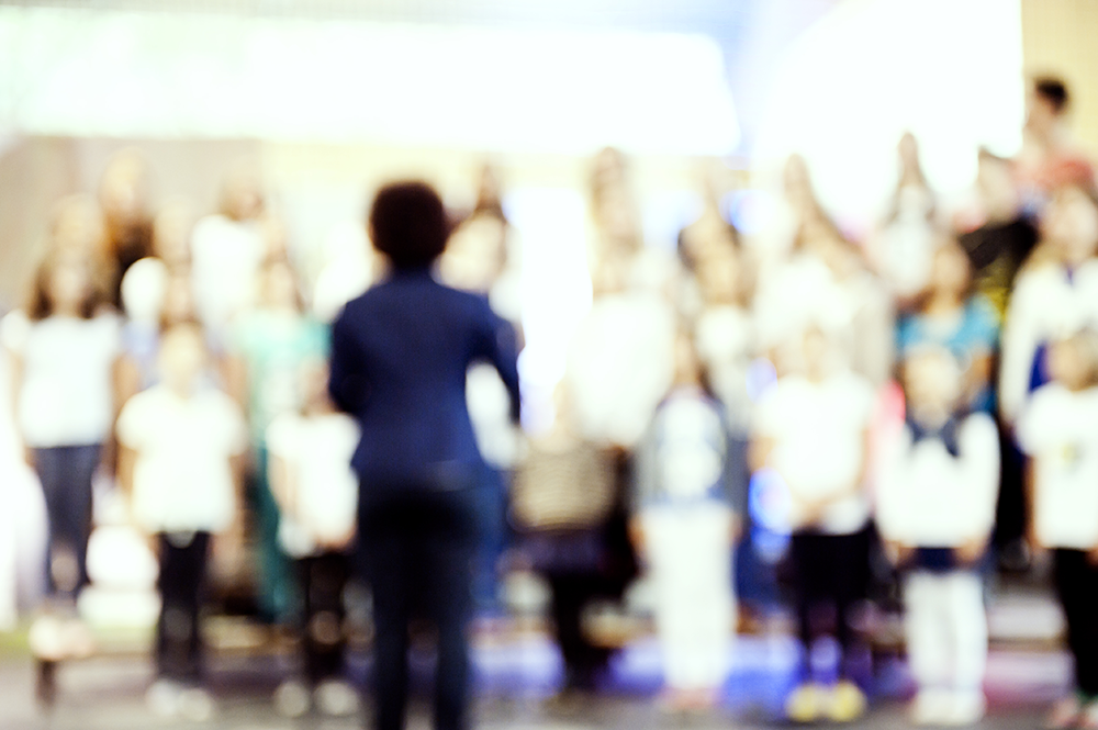 Blurred photo of a choir in rehearsal or performance with choir director.