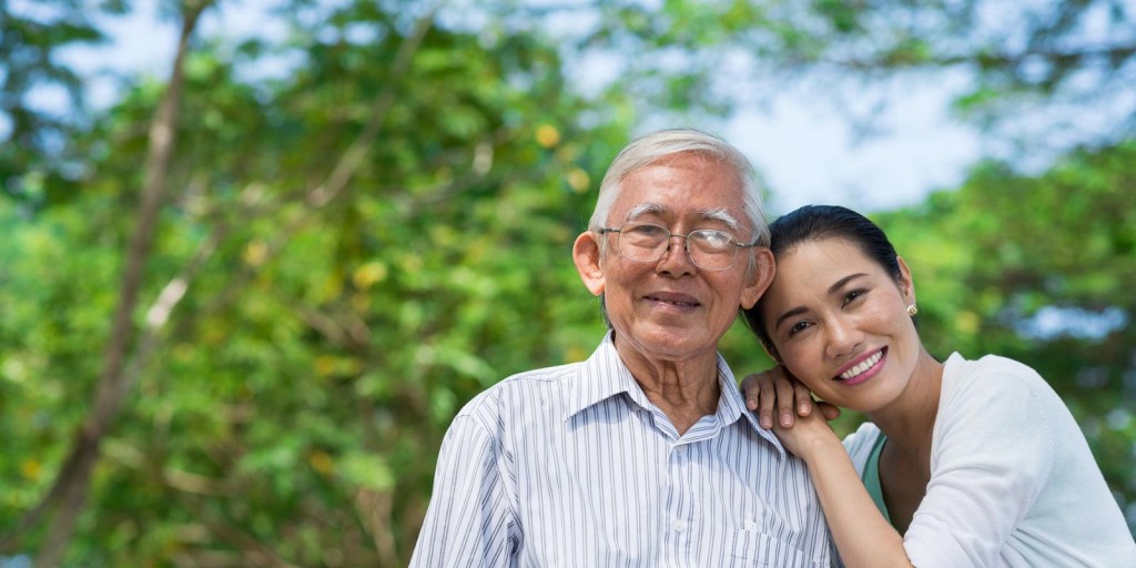 Photo shows an older man smiling with a woman leaning her head on his shoulder.